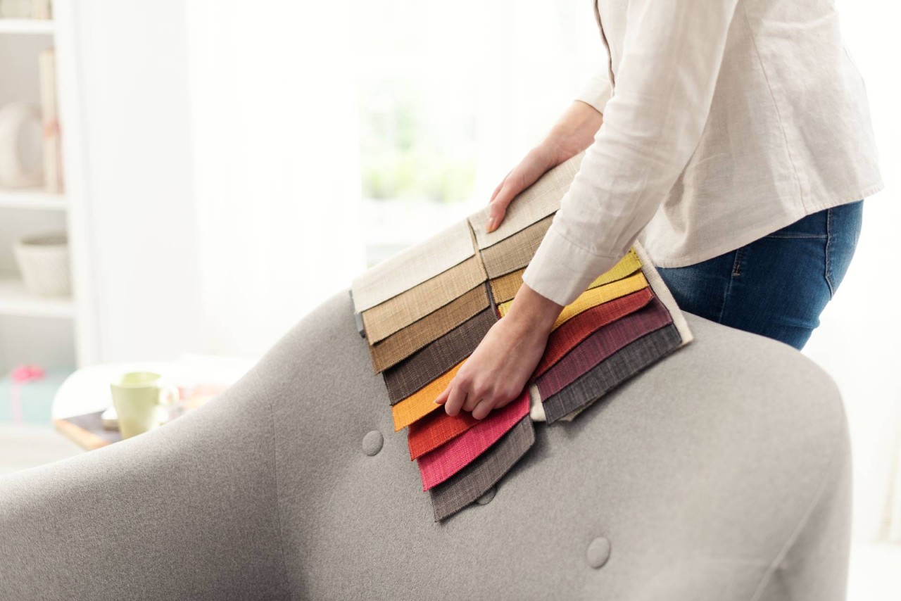 Person holding a swatch of different fabrics up against a chair to be reupholstered at Geneva’s Interiors near Federal Way, WA